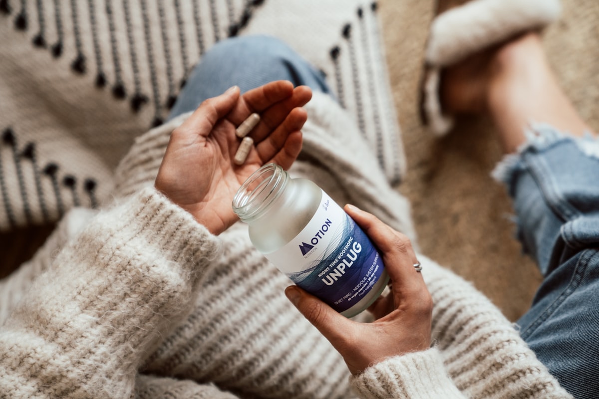 Person stretching their joints in a sunlit outdoor space while holding herbal supplements